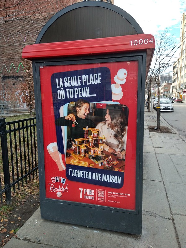 Cartel publicitario con el texto "El único sitio donde puedes comprarte una 
casa", y una foto de dos personas haciendo un castillo de naipes en un 
pub