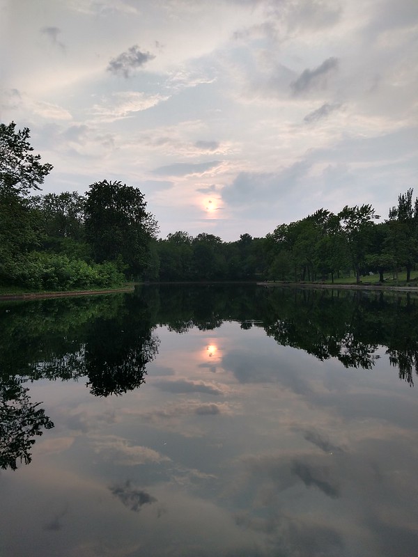 Puesta de sol, con muchas nubes, reflejada en la superficie de un 
lago
